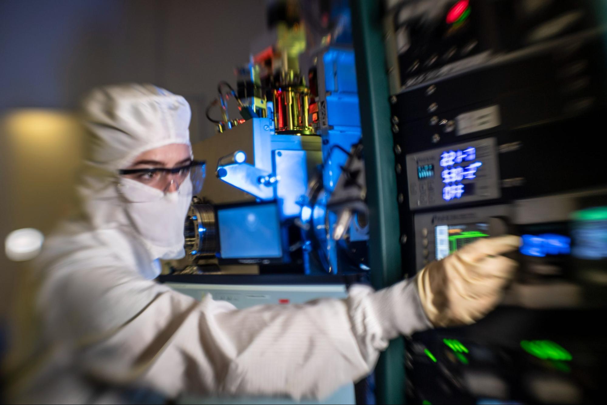Person working in a clean room environment flipping switches on a machine